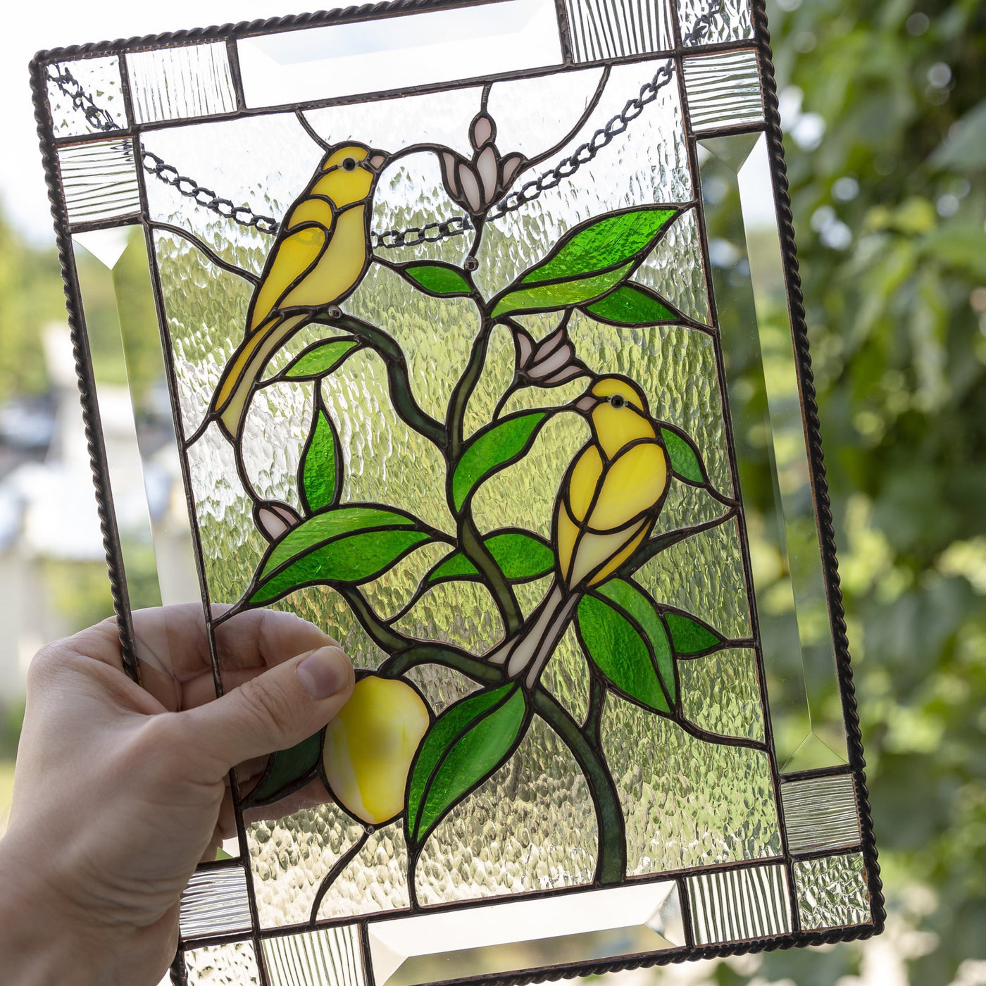Zoomed stained glass window hanging of two canary birds sitting on the lemon tree