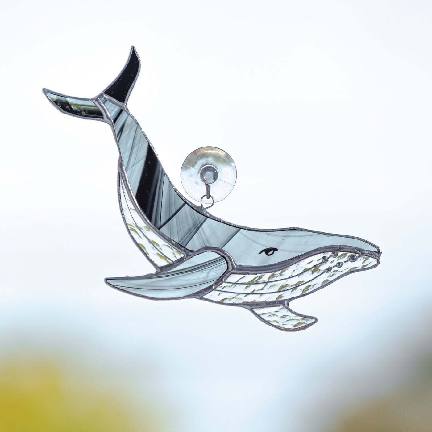 Stained glass suncatcher of a black and grey whale with clear lower part and its tail up