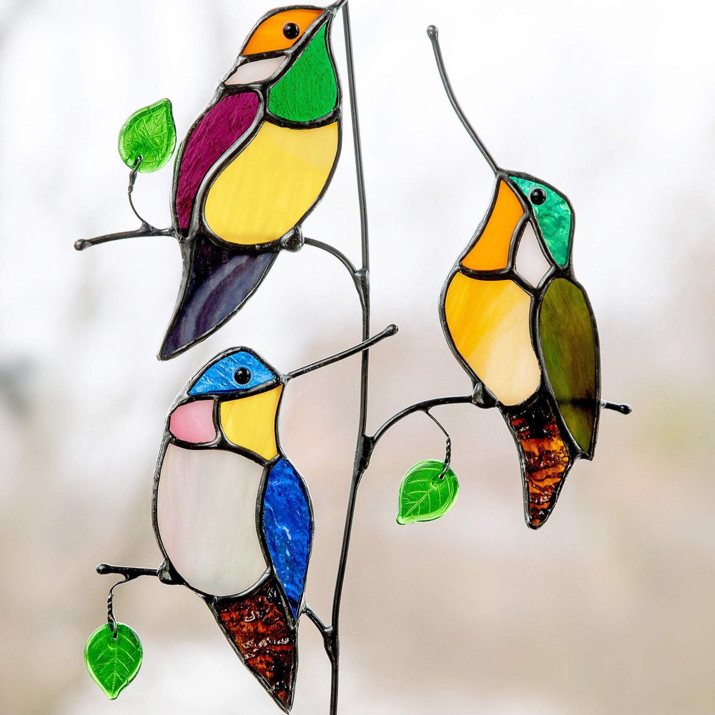Three zoomed stained glass hummingbirds on the branch with leaves suncatcher