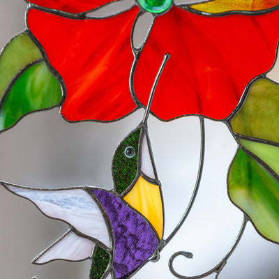 Zoomed stained glass hummingbird and red flower above it suncatcher