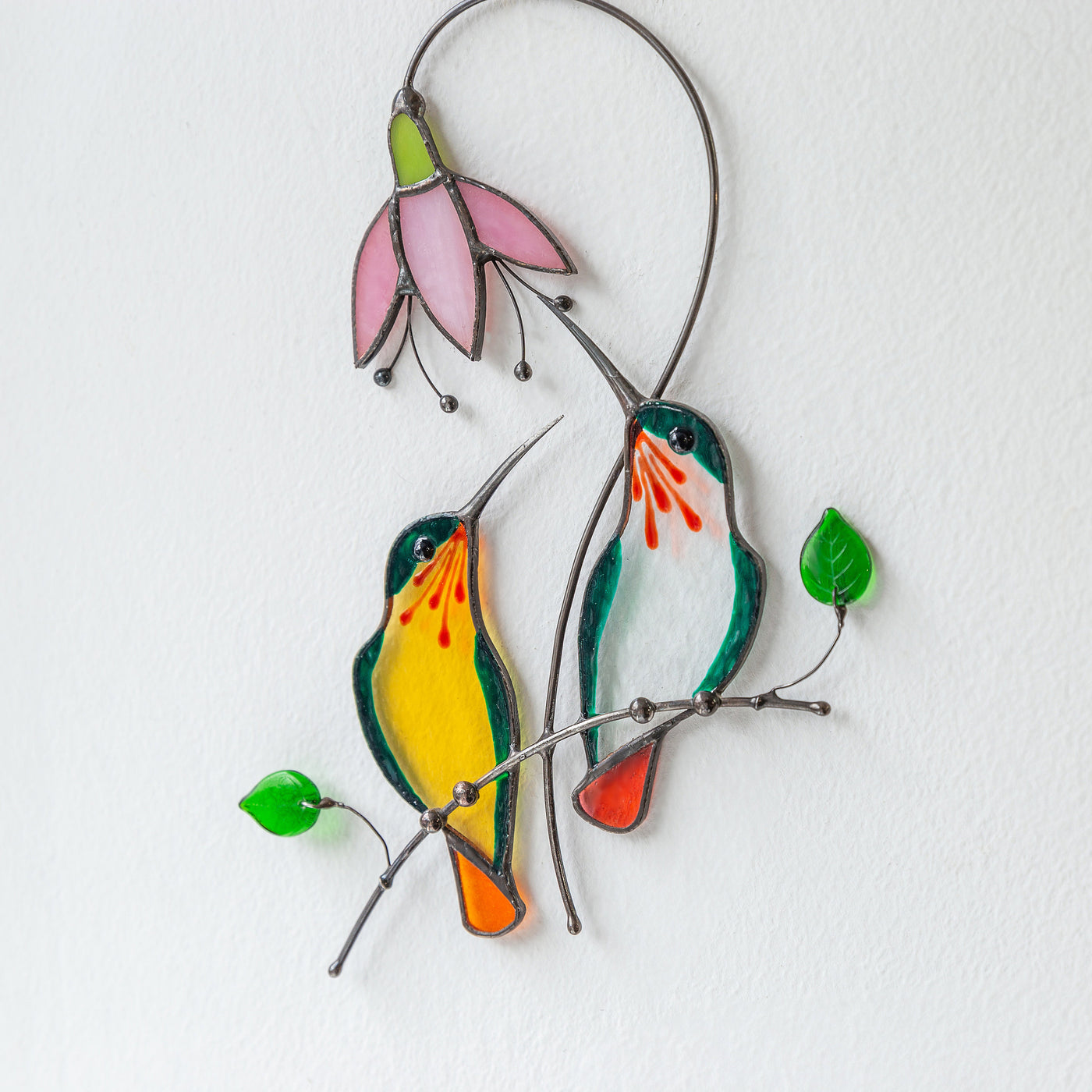 Green hummingbirds on the branch with pink flower suncatcher of stained glass