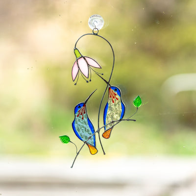 Stained glass blue hummingbirds from blue and clear glass on the branch with pink flower suncatcher