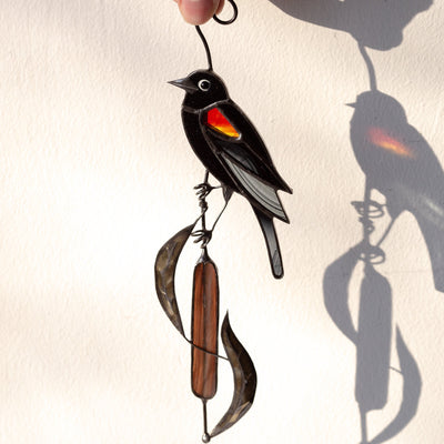 Suncatcher of a stained glass blackbird sitting on the reeds 
