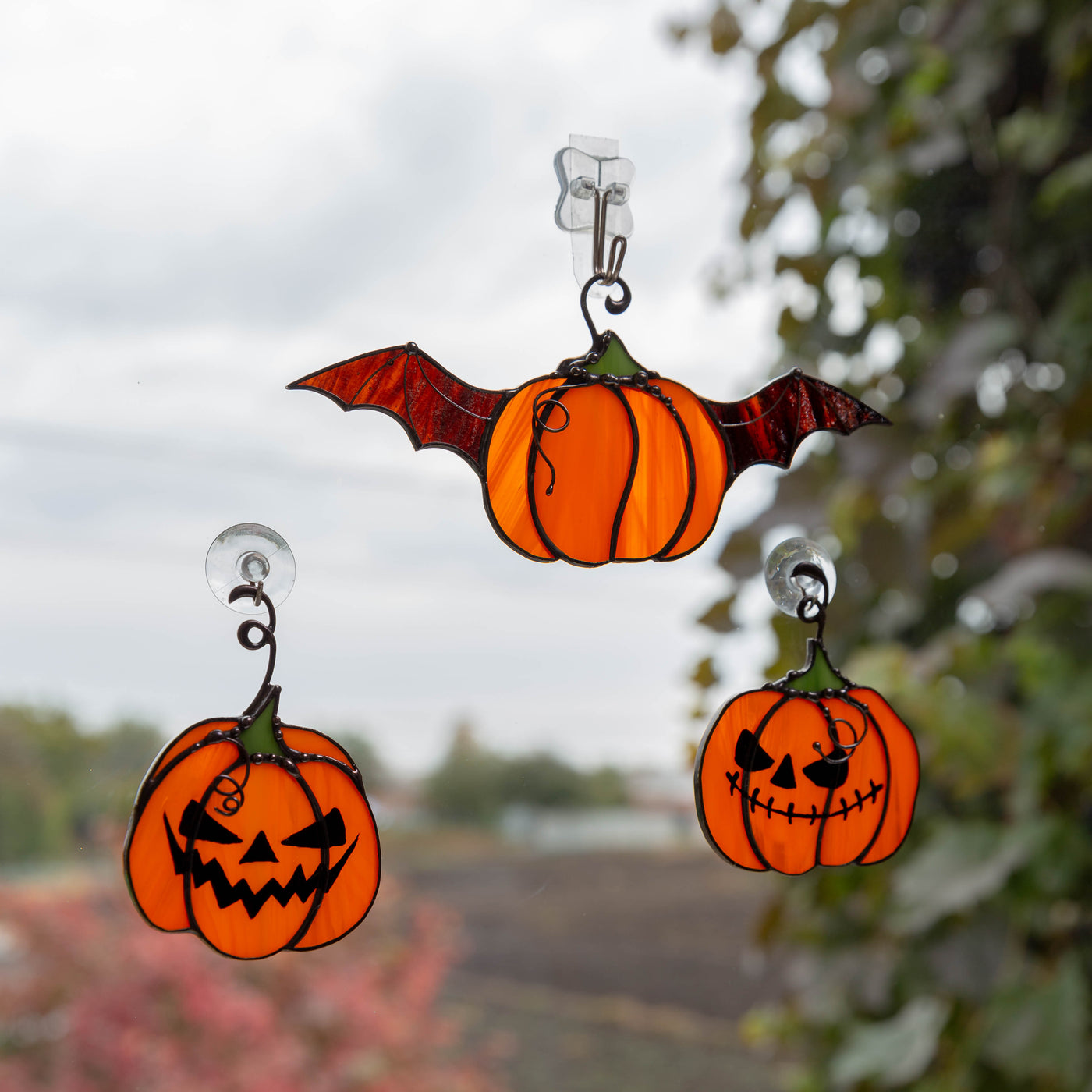 Stained glass suncatchers of two orange curved pumpkins and a flying one